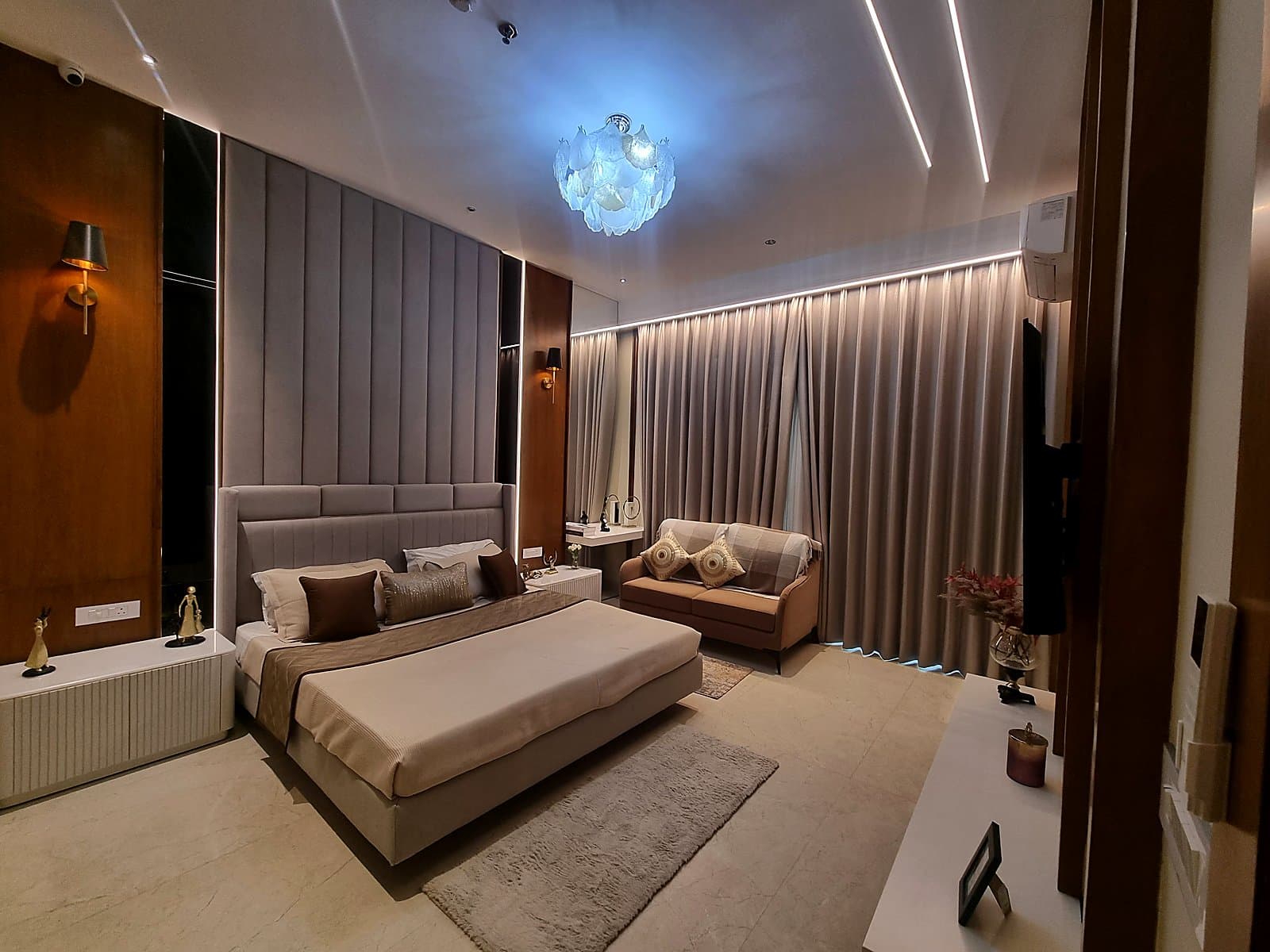 Master bedroom with upholstered headboard, designer chandelier and lounge sofa in Mohali flat