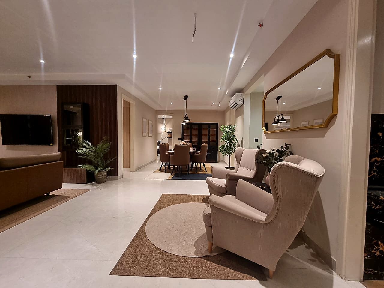 Open-plan living and dining area with wingback chairs and gold-framed mirror in Zirakpur luxury apartment
